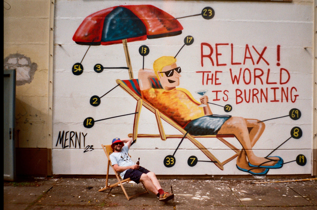 Merny artist relaxing in from of a mural he painted which is of him relaxing with the words "Relax! the world is burning"