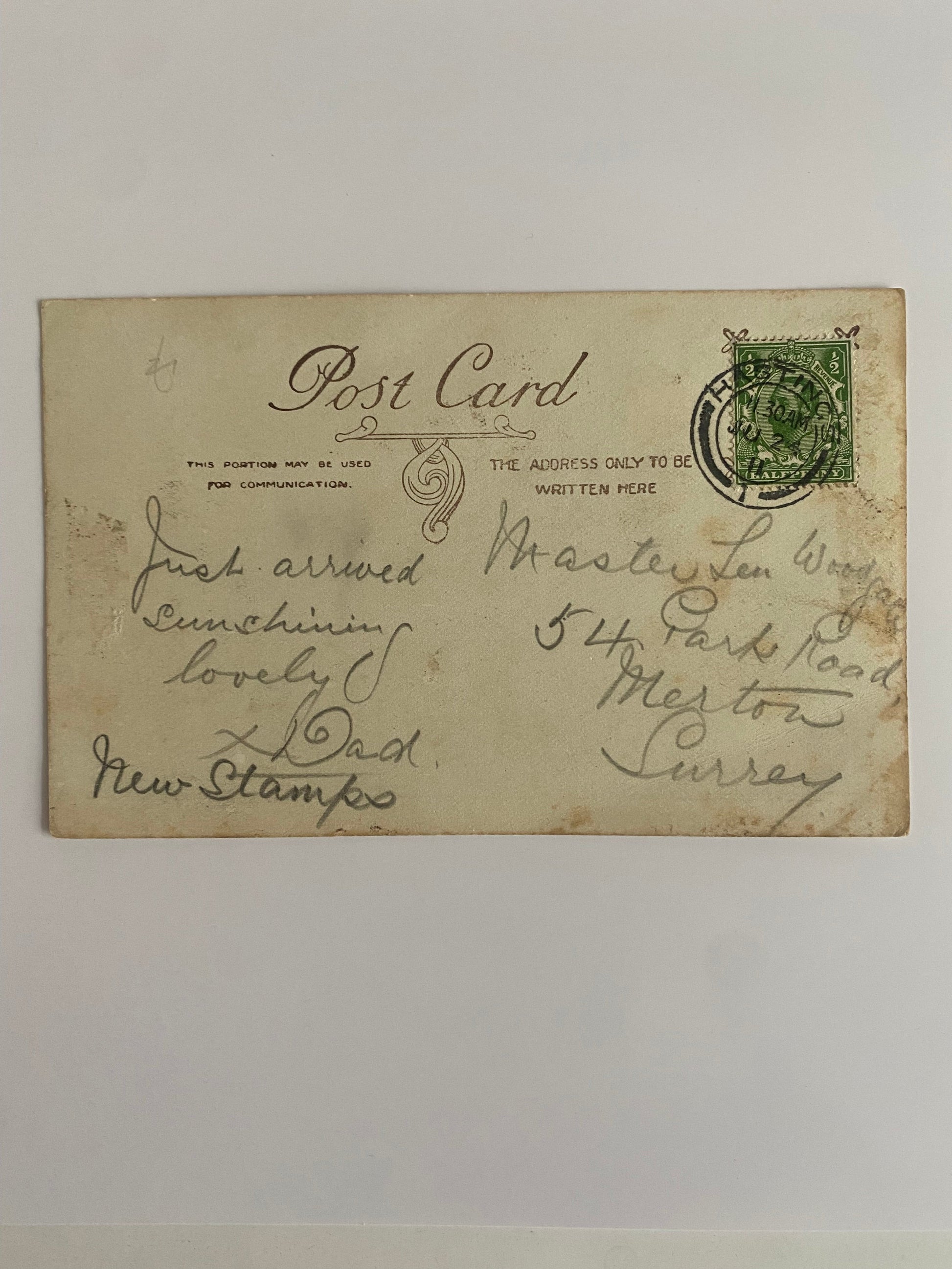 Back of a postcard with writing that says "Just arrived, sunshine lovely x Dad New Stamp". The stamp is a King George Halfpenny stamp in green with a Hastings postmark, dated 2 July 1911